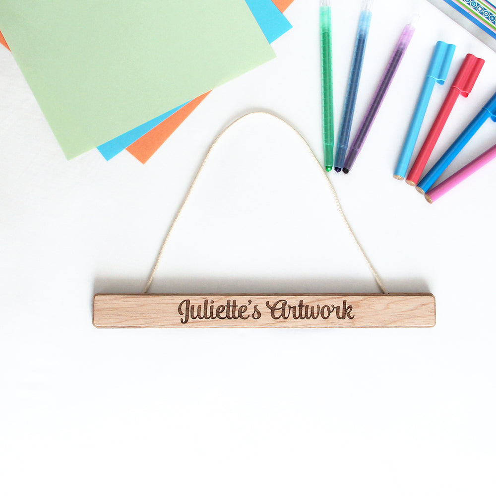 wooden artwork hanger on a white background surrounded by coloured pens and paper