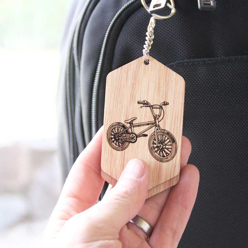 wooden id tag on a black bag. the tag has a bicycle etched on it