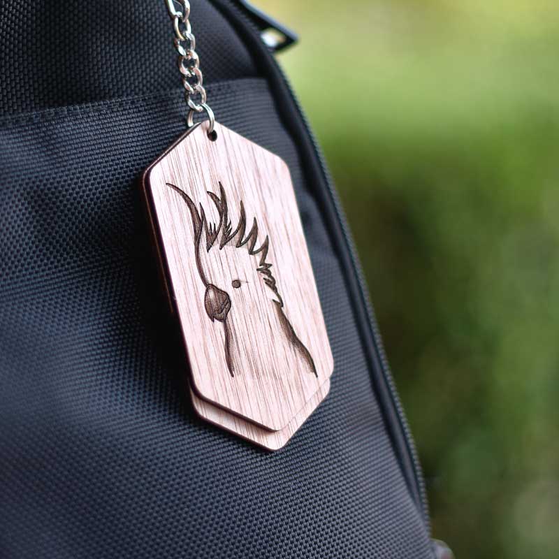 wooden bag tag with a cockatoo attached to a black bag