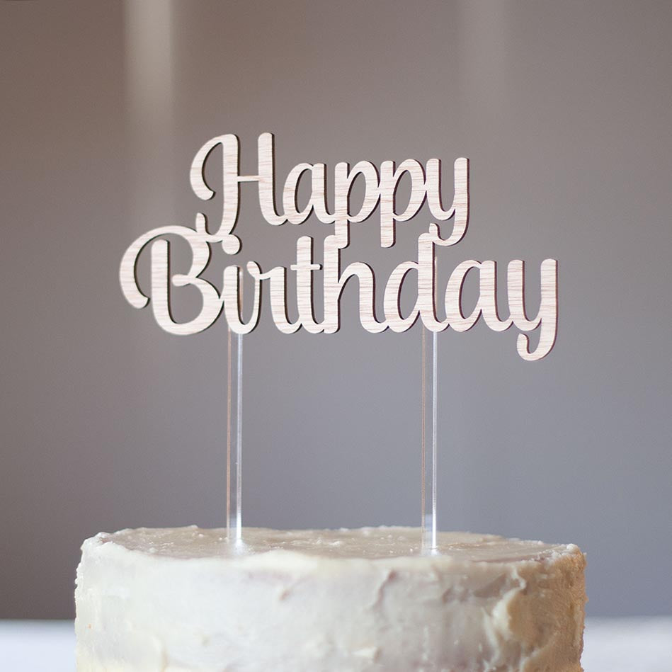 a wooden cake topper saying Happy Birthday  with two clear sticks into the cake