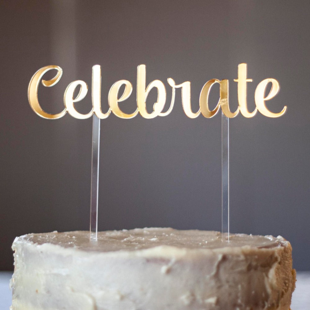 a gold mirror cake topper for a birthday or any other celebration. It says the word 'celebrate' and has two clear sticks into the cake