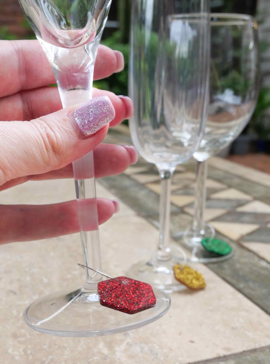 close up of a hand holding a wine glass with glitter charms around the stems