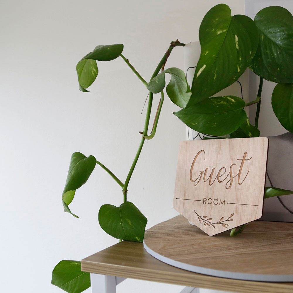 wooden hanging door sign with text "Guest room" is leaning against a plant trailing