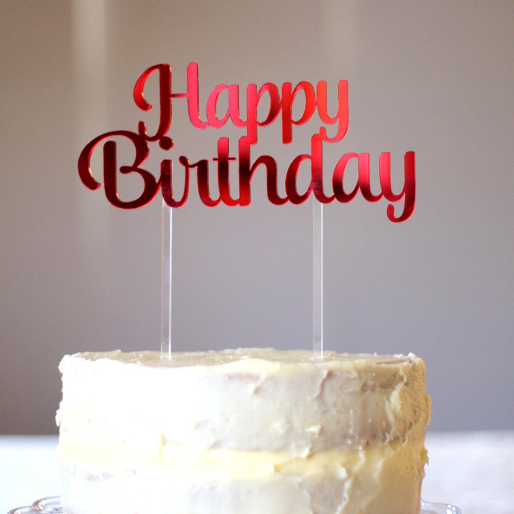 a red mirror acrylic cake topper saying Happy Birthday and two clear sticks into the cake